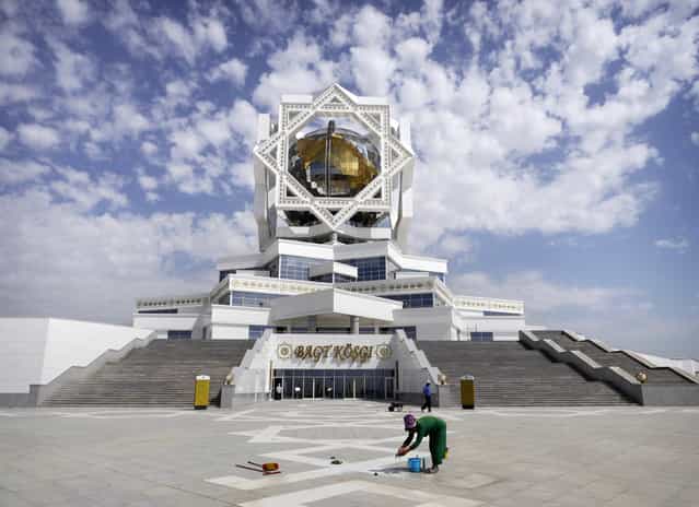 A cleaner at work in front of Ashgabat's [Palace of Happiness]. The wedding venue features a room where newlyweds are required to pose in front of a portrait of the President. Radio Free Europe subsequently dubbed Berdimuhamedow [Photobomber-in-Chief]. (Photo by Amos Chapple via The Atlantic)