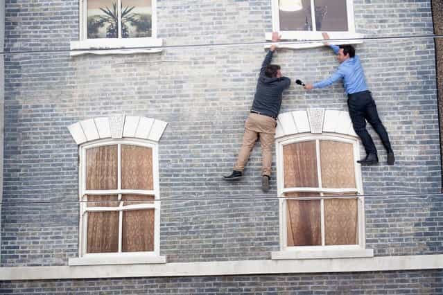 People appear dangling as a large-scale installation art piece by Leandro Erlich, named [Dalston House], is displayed on June 24, 2013 in London, England. Part of the [Beyond Barbican] summer series of events, the interactive installation is a full facade of a late nineteenth-century Victorian terraced house built on the ground with a large mirror above it to reflect people as to appear dangling from the structure. (Photo by Dan Dennison/Getty Images)