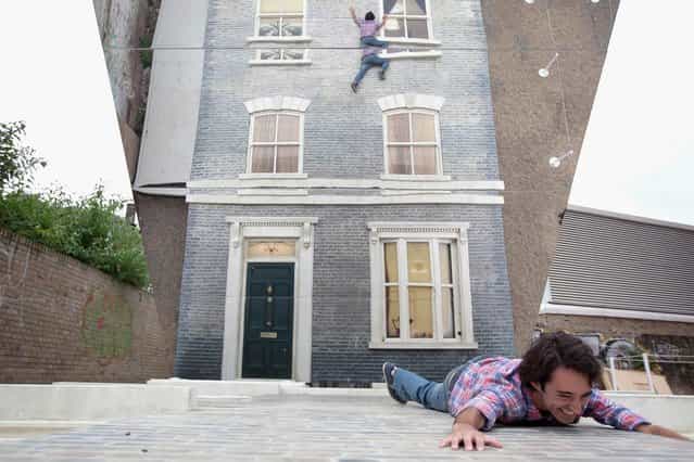 An man appears in a large-scale installation art piece by Leandro Erlich, named [Dalston House], on June 24, 2013 in London, England. Part of the [Beyond Barbican] summer series of events, the interactive installation is a full facade of a late nineteenth-century Victorian terraced house built on the ground with a large mirror above it to reflect people as to appear dangling from the structure. (Photo by Dan Dennison/Getty Images)