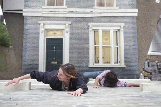 People appear dangling as a large-scale installation art piece by Leandro Erlich, named [Dalston House], is displayed on June 24, 2013 in London, England. Part of the [Beyond Barbican] summer series of events, the interactive installation is a full facade of a late nineteenth-century Victorian terraced house built on the ground with a large mirror above it to reflect people as to appear dangling from the structure. (Photo by Dan Dennison/Getty Images)