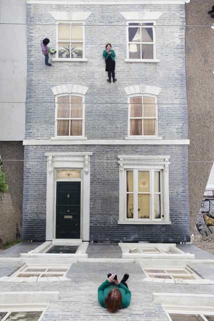 A woman appears in a large-scale installation art piece by Leandro Erlich, named [Dalston House], on June 24, 2013 in London, England. Part of the [Beyond Barbican] summer series of events, the interactive installation is a full facade of a late nineteenth-century Victorian terraced house built on the ground with a large mirror above it to reflect people as to appear dangling from the structure. (Photo by Dan Dennison/Getty Images)