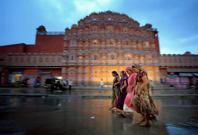 [Women in Jaipur, India]. I thought this would be a good place for pictures, so I returned during the evening on my second night in Jaipur. I got lucky with the rain because it made for interesting reflections, and I had a good time trying to capture the chaotic motion on the streets of Jaipur. Hawa Mahal (The Palace of Winds) is pictured in the background. (Photo and caption by Edward Graham/National Geographic Traveler Photo Contest)