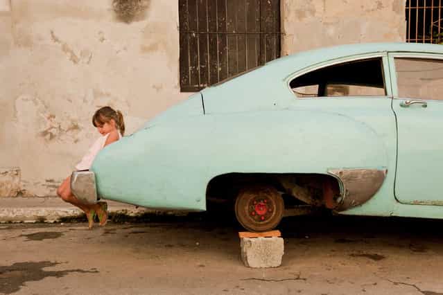 [Innocence and Icon]. The classic American car has become a symbol and staple throughout Cuba. In the back streets of Havana, one who has yet to learn of the country’s history, shows her innocence at play. (Photo and caption by Eric Kruszewski/National Geographic Traveler Photo Contest)