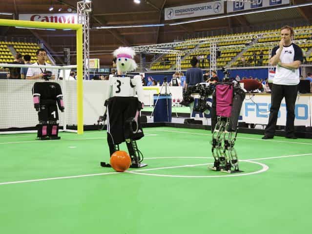 In this photo taken Thursday, June 27, 2013, a robot from the University of Bonn dribbles around a Japanese competitor at the RoboCup championships in Eindhoven, Netherlands. Around 300 teams from 40 countries are competing this week at the RoboCup. The competition has the long-term goal of building a team of androids good enough to beat the human world cup team by 2050. (Photo by Toby Sterling/AP Photo)
