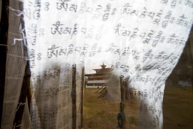 [Temple Of The Divine Madman Through Prayer Flags]. Chimi Lhakhang, or more commonly known as the Temple Of The Divine Madman, is located in the hills of the Punakha District in Bhutan. The day was gray and windy on my visit to the temple, which I had already shot once before. Trying something new, I used a wide-angle lens and the built-in flash on my Canon 7D to create a shadow on the prayer flags through which to shoot. It took a few tries as the wind whipped the flags in front of my lens. The Sanskrit mantra Om Mani Padme Hum is written over and over on the flags. (Photo and caption by Peter Carey/National Geographic Traveler Photo Contest)