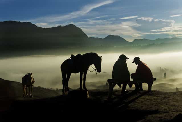 [Horsemen]. Some of the Tengger people living around Mount Bromo work as horsemen in the mornings. The job is to lead tourists on the horses as close to the crater edge as possible. While waiting for their guests to descend from the the crater edge, this pair engages in quiet contemplative conversation as sun breaks over the horizon. Location: Mount Bromo, Indonesia. (Photo and caption by Ek Teck Leow/National Geographic Traveler Photo Contest)