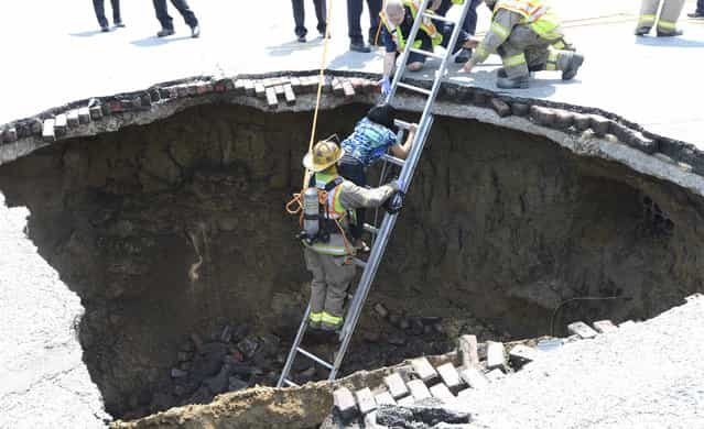 A Toledo firefighter rescues Pamela Knox after a massive sinkhole opened up underneath her car in Toledo, Ohio, on July 3, 2013. (Photo by Reuters/Lt. Matthew Hertzfeld/Toledo Fire and Rescue via The Atlantic)