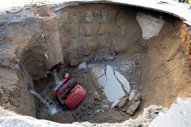 A truck lies in a sinkhole which occurred overnight on Shiliuzhuang road, in Beijing, on April 26, 2011. A section of the road collapsed beneath the truck, slightly injuring the driver and a passenger, who both jumped out the vehicle before it sank into the hole. (Photo by AFP Photo via The Atlantic)