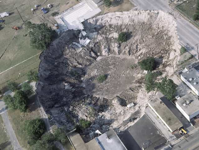 This aerial view shows a large sinkhole that claimed several sports cars, a house, and the deep end of the city swimming pool, in Winter Park, Florida, on May 11, 1981. (Photo by AP Photo via The Atlantic)