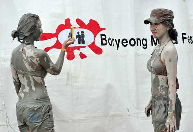 Tourists covered in mud take pictures during the 16th Boryeong mud festival at Daecheon swimming beach in Boryeong, 150 kilometers southwest of Seoul, on July 20, 2013. The annual festival which runs from July 19-28 aims to encourage the use of mud for cosmetic skin-care and to promote tourism in the region. (Photo by Jung Yeon-Je/AFP Photo)