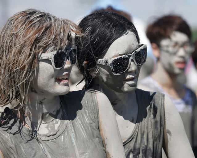 Tourists look at other festival-goers playing in the mud during the Boryeong Mud Festival at Daecheon beach in Boryeong, about 190 km (118 miles) southwest of Seoul, July 19, 2013. About 2 to 3 million domestic and international tourists visit the beach during the annual mud festival, according to the festival organisers. (Photo by Lee Jae-Won/Reuters)