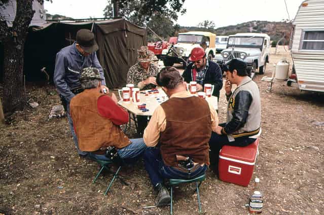 Deer hunters drink and play poker while waiting for deer. The hunters have built a permanent camp to which they return each year, November 1972. (Photo by Marc St. Gil/NARA via The Atlantic)