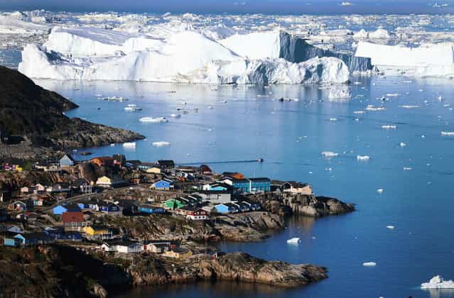 The village of Ilulissat is seen near the icebergs that broke off from the Jakobshavn Glacier, on July 24, 2013 in Ilulissat, Greenland. Researchers affiliated with the National Science Foundation and other organizations are studying the phenomena of melting glaciers and its long-term ramifications. (Photo by Joe Raedle/Getty Images via The Atlantic)