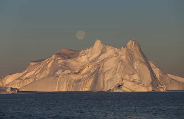 A full moon, over an iceberg from the Jakobshavn Glacier, on July 23, 2013 near Ilulissat. (Photo by Joe Raedle/Getty Images via The Atlantic)