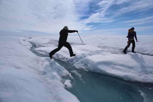 Scientist Ian Joughin of the University of Washington leaps over a small meltwater stream as he walks with Graduate Student, Laura Stevens, from the Massachusetts Institute of Technology and Woods Hole Oceanographic Institution as they conduct research on July 16, 2013 on the Glacial Ice Sheet, Greenland. (Photo by Joe Raedle/Getty Images via The Atlantic)