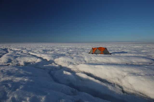 A tent, near the worksite of scientists Sarah Das from the Woods Hole Oceanographic Institution and Ian Joughin of the University of Washington along with their team, as they conduct research on July 15, 2013 on the glacial ice sheet. The scientists set up Global Positioning System sensors to closely monitor the evolution of the surface lakes and the motion of the surrounding ice sheet and have uncovered a plumbing system for the ice sheet, where meltwater can penetrate thick, cold ice and accelerate some of the large-scale summer movements of the ice sheet. (Photo by Joe Raedle/Getty Images via The Atlantic)
