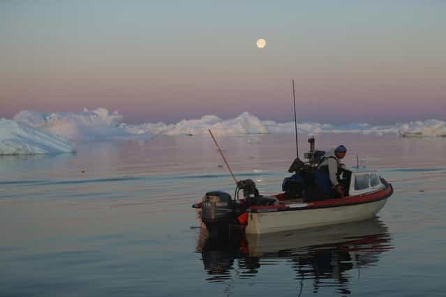 Fisherman, Inunnguaq Petersen, waits for fish to catch on the line he put out near icebergs that broke off from the Jakobshavn Glacier on July 23, 2013 in Ilulissat, Greenland. (Photo by Joe Raedle/Getty Images via The Atlantic)
