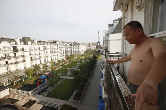 A resident stands on the balcony of his apartment at the Tianducheng development in Hangzhou, Zhejiang Province August 1, 2013. Tianducheng, developed by Zhejiang Guangsha Co. Ltd., started constructing in 2007 and was known as a knockoff of Paris with a scaled-replica of the Eiffel Tower, standing 108 metres, and Parisian houses. Although designed to accommodate at least ten thousand people, Tianducheng remains sparsely populated and is now considered as a [ghost town], according to local media. (Photo by Aly Song/Reuters)