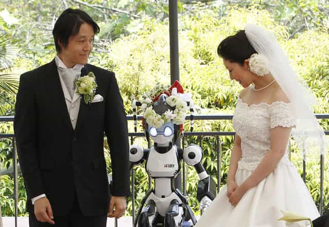A humanoid robot named [I-Fairy] (C) acts as a witness at the wedding ceremony between Tomohiro Shibata (L) and Satoko Inoue in Tokyo May 16, 2010. The couple decided to use the robot, which conducted the ceremony with its audio functions, from Inoue's company to perform the witness' duties as they first met due to common work interest related to robots. (Photo by Yuriko Nakao/Reuters)