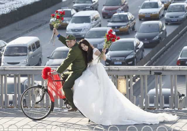 An engaged couple sits on a bicycle as they pose for wedding photographs to the theme of [naked wedding], on a pedestrian bridge on Valentine's Day in central Beijing February 14, 2011. [Naked wedding] is a popular new expression in China which means young couples get married with no houses, cars or little bank savings. (Photo by Reuters/China Daily)