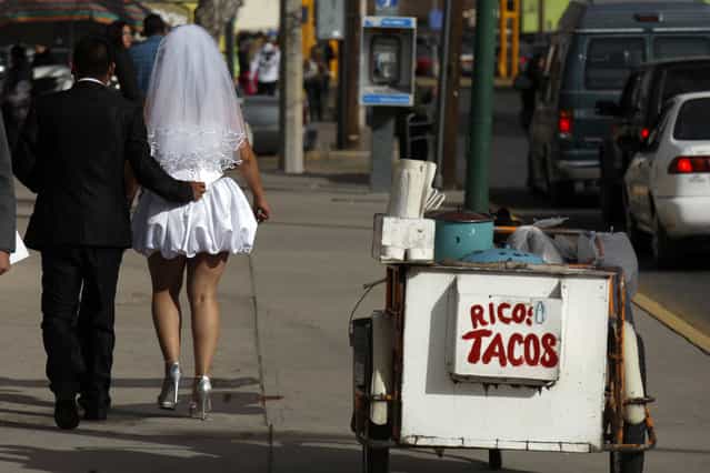 A newly married couple walks past a taco stand with the sign reading [Yummy Tacos] after a mass wedding in Ciudad Juarez February 14, 2012. The mass wedding ceremony was held for 3,121 couples on Valentine's day. (Photo by Jose Luis Gonzalez/Reuters)
