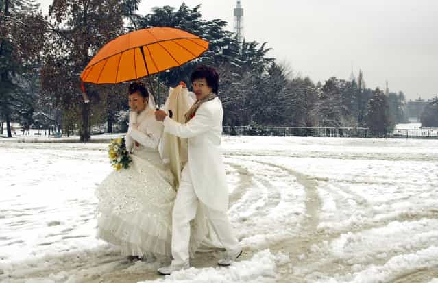 A newly wedded Chinese couple walks in the snow at a park in downtown Milan December 10, 2008. Italy has been struck by extreme weather this week, snowfall in the north, floods in Venice and strong winds fanning wildfires in the south. (Photo by Stefano Rellandini/Reuters)