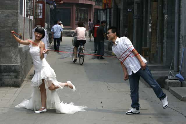 A Chinese couple pose for a wedding photo on a busy alleyway or [hutong] in Beijing July 7, 2008. Marriage registration offices in Beijing predict more than 9,000 couples will get married on August 8 this year, state media reported. The number eight is auspicious in Chinese, as it is pronounced like the word [fa], which is part of the expression meaning [to get wealthy]. The opening date of the Olympics adds new meaning, it said. (Photo by Claro Cortes IV/Reuters)