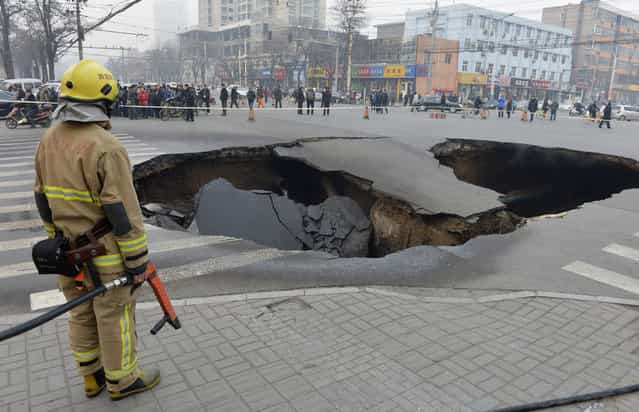 A firefighter stands next to a cave-in at a crossroad in Taiyuan, Shanxi province, December 26, 2012. The cause of the cave-in, measuring about 6 meters (20 ft.) in depth, 10 meters (32.8 ft.) in diameter, is still under investigation. Three coal gas tubes and one water tube were broken during the collapse and firefighters are trying to dilute the coal gas at the site, reported local media. (Photo by Reuters/Stringer)