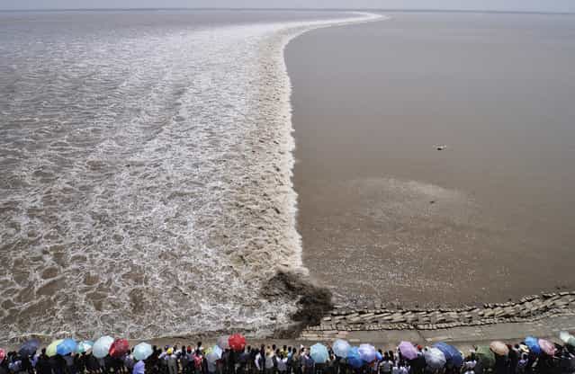 A remote controlled helicopter hovers over the Qiantang River as tourists gather on the river bank to see the soaring tide in Haining, Zhejiang province, on September 13, 2011. (Photo by Reuters/Stringer via The Atlantic)