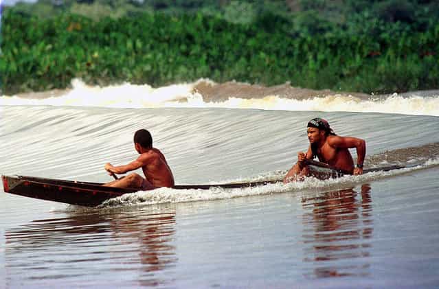 Villagers ride the Pororoca wave in a canoe as it passes near their town of Sao Domingos do Capim, northern Brazil, on March 12, 2001. (Photo by Paulo Santos/AP Photo via The Atlantic)