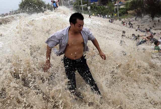 People struggle as waves from a tidal bore surge past a barrier on the banks of Qiantang River in Haining, Zhejiang province, August 22, 2013. As Typhoon Trami landed in eastern China, tidal level in Qiantang River was recorded at 6.6 metre high with surge reaching 1.3 metre high, local media reported. (Photo by Reuters/China Daily)