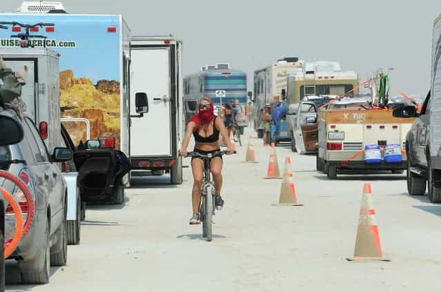 In this Aug. 26, 2013 photo, a woman rides her bike between cars waiting to enter Burning Man in Gerlach, Nev. According to The Reno Gazette-Journal, an estimated 68,000 people are anticipated to attend the event. (Photo by Andy Barron/AP Photo/Reno Gazette-Journal)