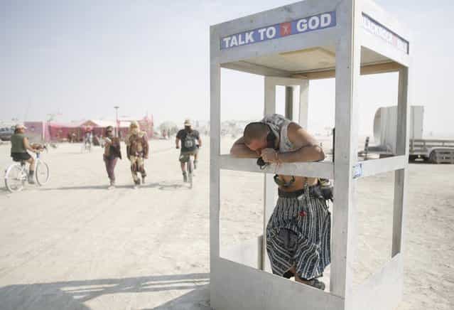 Pippin, his Playa name, chats on the phone with God during the Burning Man 2013 arts and music festival in the Black Rock Desert of Nevada, September 1, 2013. The federal government issued a permit for 68,000 people from all over the world to gather at the sold out festival, which is celebrating its 27th year, to spend a week in the remote desert cut off from much of the outside world to experience art, music and the unique community that develops. (Photo by Jim Urquhart/Reuters)