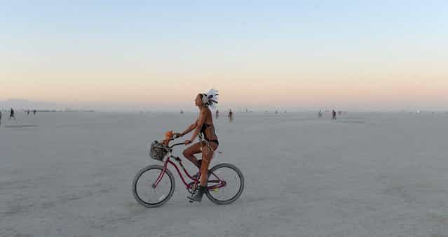 A woman rides a bicycle on the playa after sunset at the Burning Man festival in Gerlach, Nev. on Friday, Aug. 30, 2013. Once a year, tens of thousands of participants gather in Nevada's Black Rock Desert for the counterculture event. (Photo by Andy Barron/AP Photo/Reno Gazette-Journal)