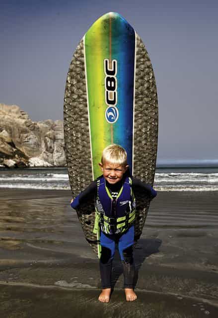 Triston poses for a photo with his surfboard before catching some waves with his father. (Photo by Joe Johnston/The Tribune of San Luis Obispo)