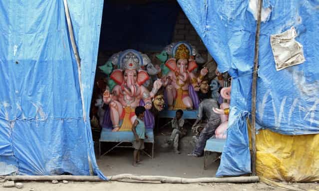 Indian children stand near idols of elephant-headed Hindu God Ganesha being prepared for Ganesh Chaturthi festival at a workshop in Hyderabad, India, Thursday, September 5, 2013. Ganesh Chaturthi, which begins from September 9, is celebrated as the birthday of Lord Ganesha who is widely worshiped by Hindus as the god of wisdom, prosperity and good fortune. (Photo by Mahesh Kumar A./AP Photo)