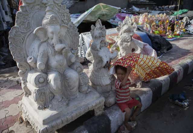 An Indian child plays in front of Ganesh statues being sold near the road ahead of the Ganesh Chaturthi festival in New Delhi on September 2, 2013. The Hindu festival which celebrates the rebirth of the God Lord Ganesha, starts September 9 and culminates on September 19, with many of the statues being immersed in bodies of water. (Photo by Andrew Caballero-Reynolds/AFP Photo)
