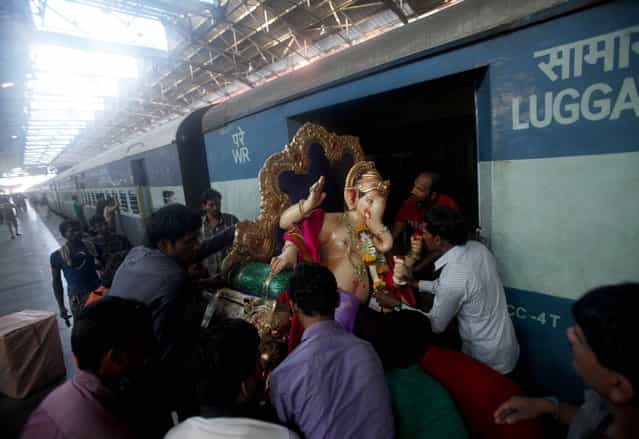 A clay idol of elephant headed Hindu god Ganesh is carried onto a passenger train before being transported to a place of worship in Mumbai, India, Sunday, September1, 2013. Ganesh Chaturthi, celebrated as the birthday of Lord Ganesha, begins September 9. The idols will be immersed in water bodies at the end of the festival. (Photo by Rafiq Maqbool/AP Photo)