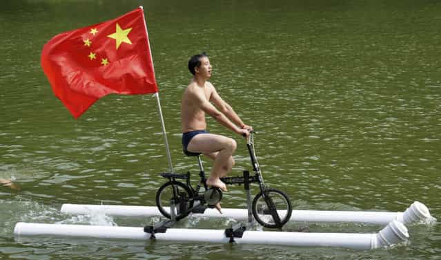 A Chinese flag is seen as Liu Wanyong performs on his invention, an improvised bicycle which is held afloat by plastic tubes, in Zhenning, Guizhou province, August 29, 2013. Liu, 52, is a grassroots inventor who mostly creates things that are related with the traditional village lives of the ethnic minority people in Guizhou. (Photo by Reuters/Stringer)