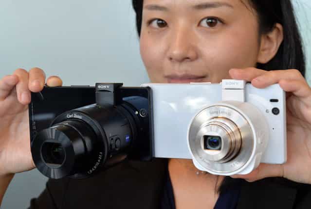 A Japan's electronics giant Sony employee displays the new concept digital camera [Cyber-shot DSC-QX100] (L) and [Cyber-shot DSC-QX10], called lens-style cameras, which can turn a smartphone into a full digital camera, at the company's headquarters in Tokyo on September 12, 2013. The DSC-QX100, equipped with a 20 mega-pixel image sensor, can be operated from the smartphone with Wi-Fi connection, and will hit the market on October 25. (Photo by Yoshikazu Tsuno/AFP Photo)
