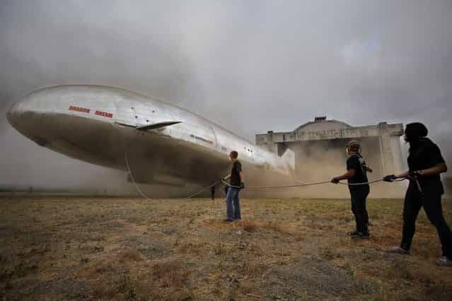 Dust flies and ground crew members slacken a tether rope while the new Aeroscraft airship conducts hover tests outside a WWII-era blimp hanger in California. September 12th, 2013. (Photo by Caters News Agency)