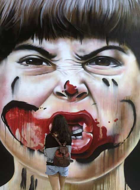 A visitor observes a work by Zack during the Art Rua street art festival in Rio de Janeiro, on September 7, 2013. (Photo by Ricardo Moraes/Reuters)