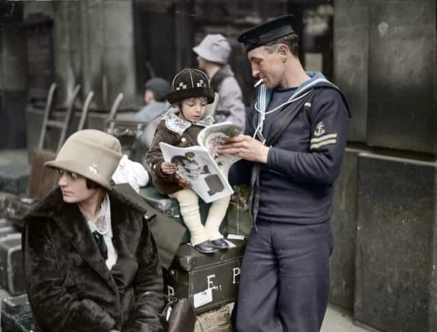 A sailor reads with his child as he waits for a holiday train at Waterloo station in London in 1927.