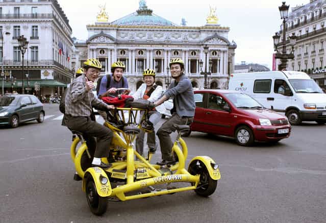 Tourists pass by the Paris Opera on a Velovisit in Paris April 24, 2006. The bike has seven seats designed for a driver and six passengers who sit in a circle and chat while pedalling. The driver holds the handlebars, which look more like a steering wheel, and is responsible for braking. The Velovisit can be hired for a tour through Paris, with or without a guide. (Photo by Charles Platiau/Reuters)
