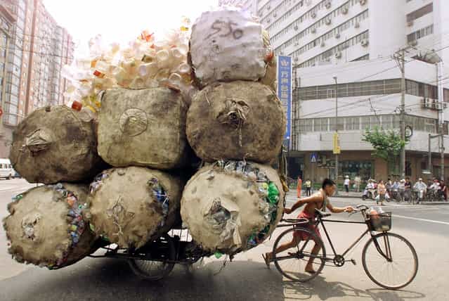 An enterprising Chinese man pulls a bicycle cart packed high with bags of recyclable plastic containers in Shanghai July 25, 2002. The man sells each kilogram (2.2 pounds) of plastic for 0.08 yuan ($.01) to a nearby depot. (Photo by Claro Cortes IV/Reuters)