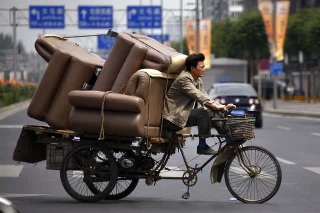 A man rides a tricycle loaded with lounge chairs along a road in Beijing June 5, 2012. (Photo by David Gray/Reuters)