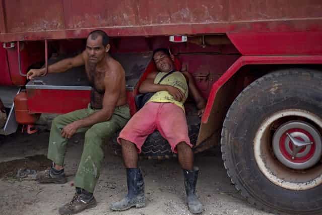 In this September 30, 2013 photo, men rest on their truck loaded with fruits and vegetables as they wait for the 114th Street Market to open on the outskirts of Havana, Cuba. Exhausted from being on the road all night, drivers grab a few winks wherever they can – atop their cabs, on rickety cots, even in wheel wells. (Photo by Ramon Espinosa/AP Photo)