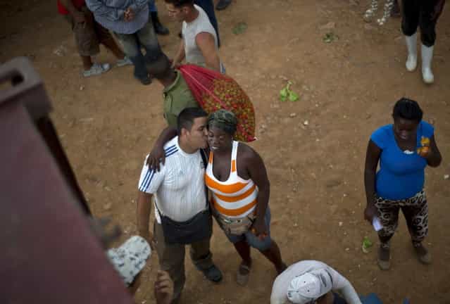 In this September 30, 2013 photo, a vegetable salesman kisses another vendor at the 114th Street Market on the outskirts of Havana, Cuba. Restaurateurs and street vendors shop here, as well as individual consumers, families and even groups of neighbors who pool their money to buy in bulk. (Photo by Ramon Espinosa/AP Photo)