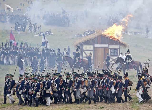 Troops march in front of a burning house during the reconstruction of the Battle of the Nations at the 200th anniversary near Leipzig, central Germany, Sunday, October 20, 2013. Some 6,000 members of military-historic associations from 24 countries took part in this performance. The Battle of Nations, from October 16-19, 1813, was fought by the coalition armies of Russia, Prussia, Austria and Sweden against the French army of Napoleon. The battle decided that Napoleon had to retreat to France. (Photo by Jens Meyer/AP Photo)