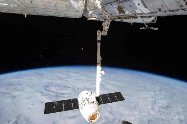 This image provided by NASA is one of a series of still photos documenting the process to release the SpaceX Dragon-2 spacecraft from the International Space Station, on March 26, 2013. The spacecraft, filled with experiments and old supplies, can be seen in the grasp of the Space Station Remote Manipulator System's robot arm or CanadArm2 after it was undocked from the orbital outpost. The Dragon was scheduled to make a landing in the Pacific Ocean, off the coast of California, later in the day. The moon can be seen at center. (Photo by AP Photo/NASA)